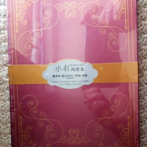 K&ouml;nnte beinhalten: Ein rotes Aquarell-Skizzenbuch mit goldenen Akzenten und dem Text "Watercolour 水彩风琴本 鲁本斯(星空系列)/棉浆/细纹 14.8cm x 21cm(原件) Cotton/300gsm/Hot pressed" auf dem vorderen Umschlag.