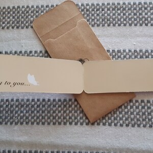 May include: A beige bookmark with a green and black butterfly on each end. The bookmark is folded in half and says "Fly to you..." on the front.