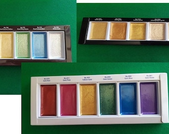 Puede incluir: Conjunto de pinturas de acuarela en varios colores, incluyendo rosa perla, rojo escarlata y amarillo limón. Las pinturas están dispuestas en pastillas rectangulares dentro de una bandeja negra y blanca, para artistas.