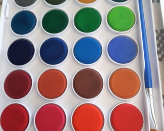 May include: A white plastic watercolor paint set with 24 round paint pans. The pans are arranged in a grid pattern and contain various colors, including black, brown, green, blue, orange, red, and pink. A blue and white paintbrush is included.