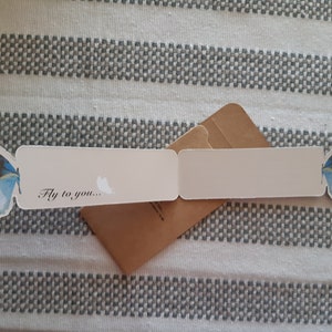 May include: A white card with a blue and brown butterfly on each side. The card is folded in half and has the text "Fly to you..." on the front.