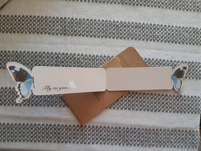 May include: A white card with a blue and brown butterfly on each side. The card is folded in half and has the text "Fly to you..." on the front.