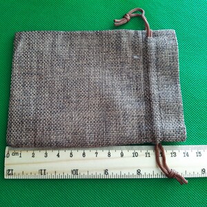 May include: A brown burlap drawstring pouch with a brown cord. The pouch is 13 cm wide and 10 cm tall.