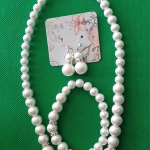May include: A white pearl necklace, bracelet and earrings set. The necklace and bracelet are made of faux pearls and the earrings are simple pearl studs.