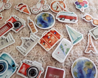 Op de afbeelding: Een verzameling kleurrijke stickers met een reisthema met afbeeldingen van een paspoort, een koffer, een camera, een wereldbol, een rode dubbeldekkerbus, een zeilboot, een kompas, de Eiffeltoren, Big Ben, een rode telefooncel, een fiets, een luchtballon en de Taj Mahal.