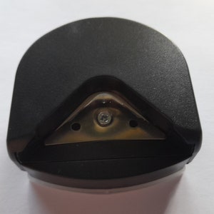 May include: Black plastic corner rounder with a metal blade. The blade has three holes and a screw in the center.