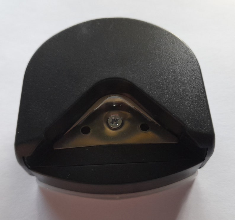 May include: Black plastic corner rounder with a metal blade. The blade has three holes and a screw in the center.