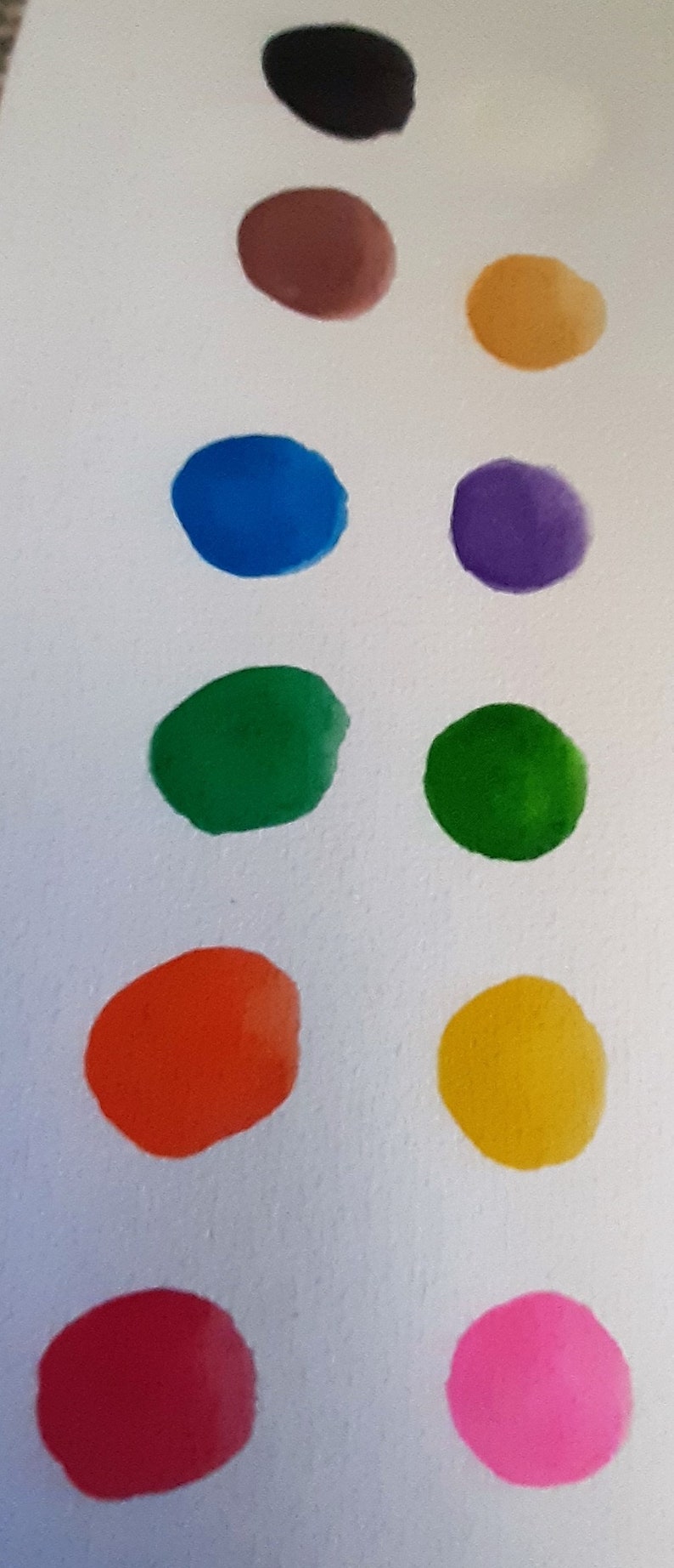 May include: A row of ten colorful paint swatches on a white surface. The swatches are arranged in a vertical line from top to bottom. The colors are black, brown, gold, blue, purple, green, green, orange, yellow, red, and pink.