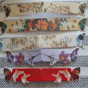May include: Six colorful bookmarks with butterfly designs and floral patterns. The bookmarks have inspirational quotes, including "My heart flutters with love".