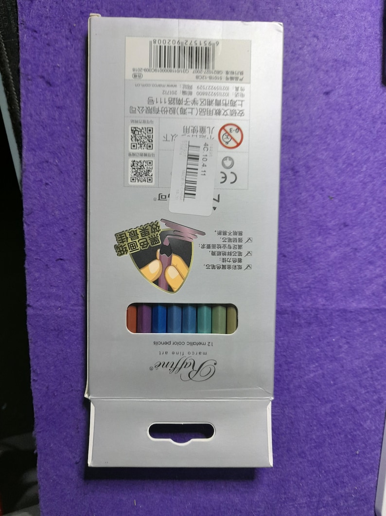 Pu&ograve; includere: Una scatola argentata con una finestra in plastica trasparente che mostra 12 matite colorate metallizzate. La scatola ha una maniglia nella parte superiore e il testo "Raffine marco fine art 12 metallic color pencils" stampato sul davanti.