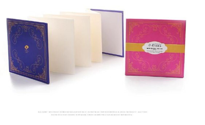 K&ouml;nnte beinhalten: Ein Satz leerer Gru&szlig;karten mit dekorativen Umschl&auml;gen. Die Umschl&auml;ge zeigen ein blaues und goldenes Design mit einem floralen Muster und ein rosafarbenes und goldenes Design mit einem floralen Muster. Der Text auf dem rosafarbenen Umschlag lautet "永生花束", was mit "Ewiger Strau&szlig;" &uuml;bersetzt wird.