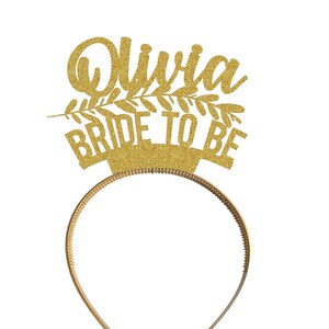 May include: Gold glitter headband with the text "Olivia Bride to Be" and a leafy design.