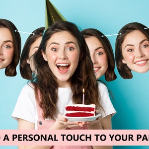 May include: A birthday party banner with a person's face printed on each flag. The banner is strung with white string and the flags are shaped like heads. The person in the photo is holding a red velvet cake with a lit candle on top.