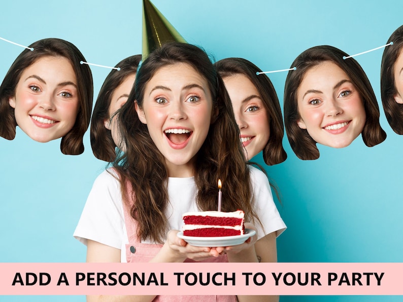 May include: A birthday party banner with a person's face printed on each flag. The banner is strung with white string and the flags are shaped like heads. The person in the photo is holding a red velvet cake with a lit candle on top.
