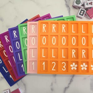 May include: A collection of colorful, rectangular game tiles, each with a grid of squares containing letters, numbers, and floral symbols. The tiles are in shades of red, purple, green, pink, and orange. Mahjong tiles are visible in the background.