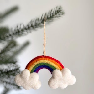 Może przedstawiać: Filcowa ozdoba w kształcie tęczy z czerwonymi, pomarańczowymi, żółtymi, zielonymi, niebieskimi i fioletowymi łukami. Dwa puszyste, białe obłoki u podstawy. Ozdoba zawieszona na naturalnym sznurku, idealna na święta.