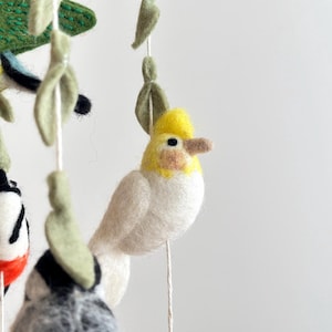 Puede incluir: Un p&aacute;jaro de fieltro blanco y amarillo con una cresta amarilla que cuelga de un m&oacute;vil. El p&aacute;jaro tiene un cuerpo blanco y una cabeza amarilla con un ojo negro. El p&aacute;jaro est&aacute; colgado de una cuerda blanca.