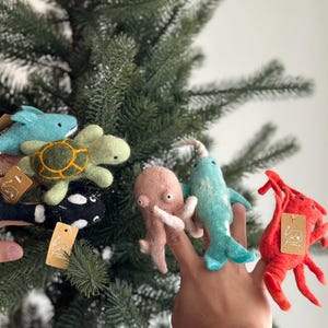 May include: A set of felt finger puppets featuring various sea creatures, including a blue whale, a green turtle, a pink octopus, a blue narwhal, and a red lobster.