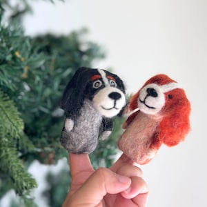 May include: Two felt finger puppets shaped like dogs. One is black and white with a brown nose and the other is orange and white with a brown nose.