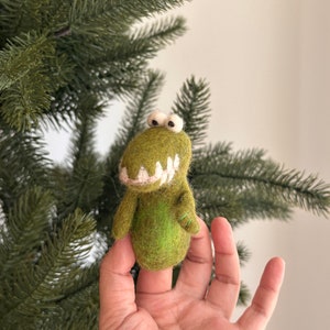 May include: A green felt finger puppet shaped like an alligator with white teeth and large white eyes.