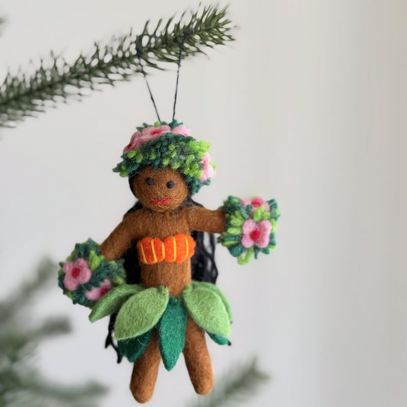 A felt ornament of a hula dancer with a green lei, orange top, and green grass skirt. The ornament has black hair and a smiling face.