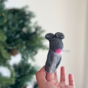 May include: A gray felt finger puppet shaped like a mouse with a pink nose. The mouse is looking directly at the camera.