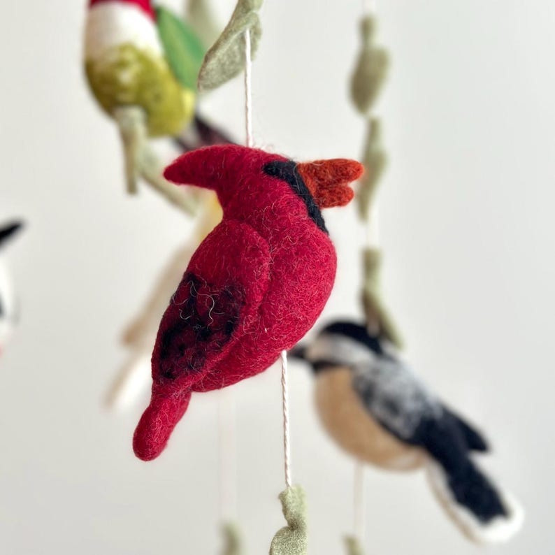 Puede incluir: Un p&aacute;jaro cardenal rojo con marcas negras cuelga de un m&oacute;vil. El p&aacute;jaro est&aacute; hecho de fieltro y tiene un peque&ntilde;o pico.
