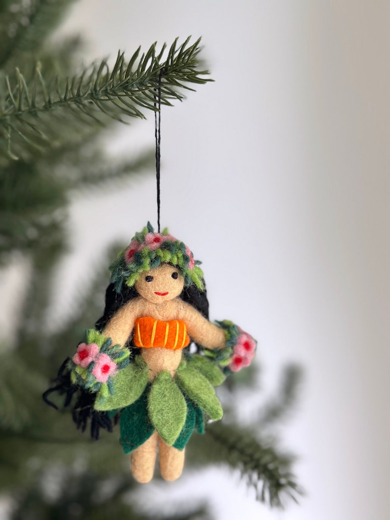 A felt ornament of a hula dancer with a green lei, orange top, and green grass skirt. The ornament has black hair and a smiling face.