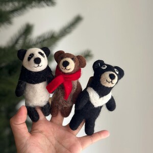 May include: Three felt finger puppets: a panda, a brown bear wearing a red scarf, and a black bear. The puppets are on a person's hand.