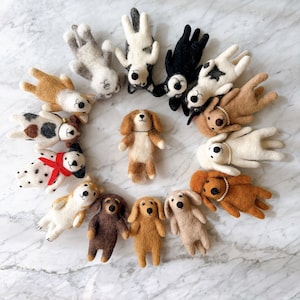 May include: A collection of 13 felt dog toys in various colors and poses. The toys are arranged in a circle on a white marble surface.