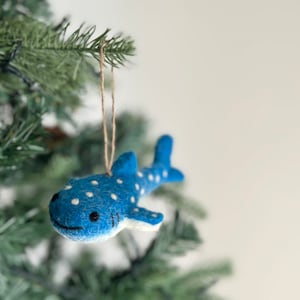 May include: A blue felt whale shark ornament with white spots hanging from a brown twine string on a green Christmas tree.