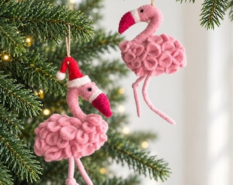 Può includere: Due decorazioni in feltro a forma di fenicottero appese a un albero. Un fenicottero indossa un cappello da Babbo Natale rosso e bianco. Entrambi hanno corpi rosa testurizzati, zampe lunghe e sottili e becchi scuri con dettagli bianchi.