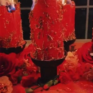 May include: Burning red pillar candles with gold accents, set in black holders, surrounded by red roses and petals. The candles are lit, with visible flames. A decorative and romantic theme.