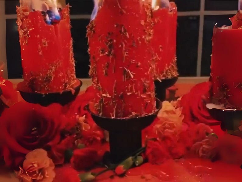 May include: Burning red pillar candles with gold accents, set in black holders, surrounded by red roses and petals. The candles are lit, with visible flames. A decorative and romantic theme.