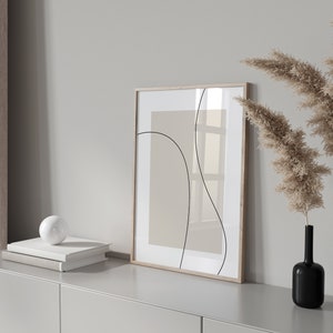 Peut inclure: Une impression abstraite encadr&eacute;e avec des lignes noires sur un fond beige est accroch&eacute;e &agrave; un mur blanc au-dessus d'une commode gris clair. Deux vases noirs avec de l'herbe de pampa s&eacute;ch&eacute;e sont sur la commode.