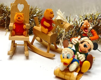 May include: A set of four wooden Christmas ornaments featuring Winnie the Pooh, Mickey Mouse, Donald Duck, and Goofy. The ornaments are painted in bright colors and depict the characters in various holiday-themed activities.