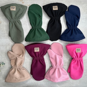 Può includere: Una collezione di otto guanti per bambini in vari colori, tra cui verde oliva, verde foresta, nero, blu navy, beige, bordeaux, rosa chiaro e rosa acceso. Ogni guanto ha un polso arricciato e un'etichetta con "BRAUN KIDS WEAR".