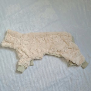 May include: A cream-colored, fluffy dog sweater with a high neck and a zipper closure.