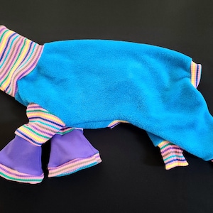 May include: A blue pet jumpsuit with purple bell bottoms. The cuffs and neck are striped with yellow, pink, green, and purple. The jumpsuit is made of a soft, plush material.