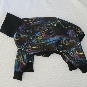 Könnte beinhalten: Schwarzer Tier-Overall mit einem farbenfrohen, wirbelnden Muster aus Blau, Lila, Gelb und Grün. Der Overall hat einen schwarzen Rollkragen und schwarze Bündchen an Ärmeln und Beinen. Der Stoff hat einen Marmoreffekt.