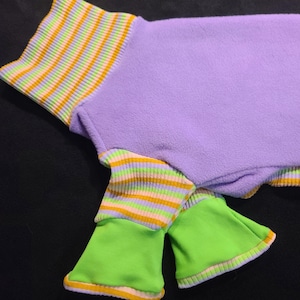 May include: A purple fleece garment with striped cuffs in green, yellow, and orange. The sleeves are bright green with orange trim. The garment is designed for a pet.