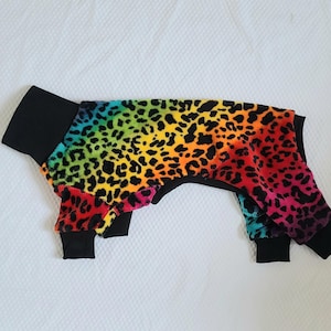 May include: Rainbow leopard print dog jumpsuit with black trim. The jumpsuit has a hood and is made of a soft, comfortable fabric.