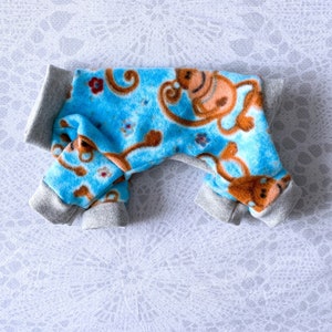 May include: A blue and grey dog onesie with a monkey print. The onesie has a grey trim around the neck, legs, and tail.