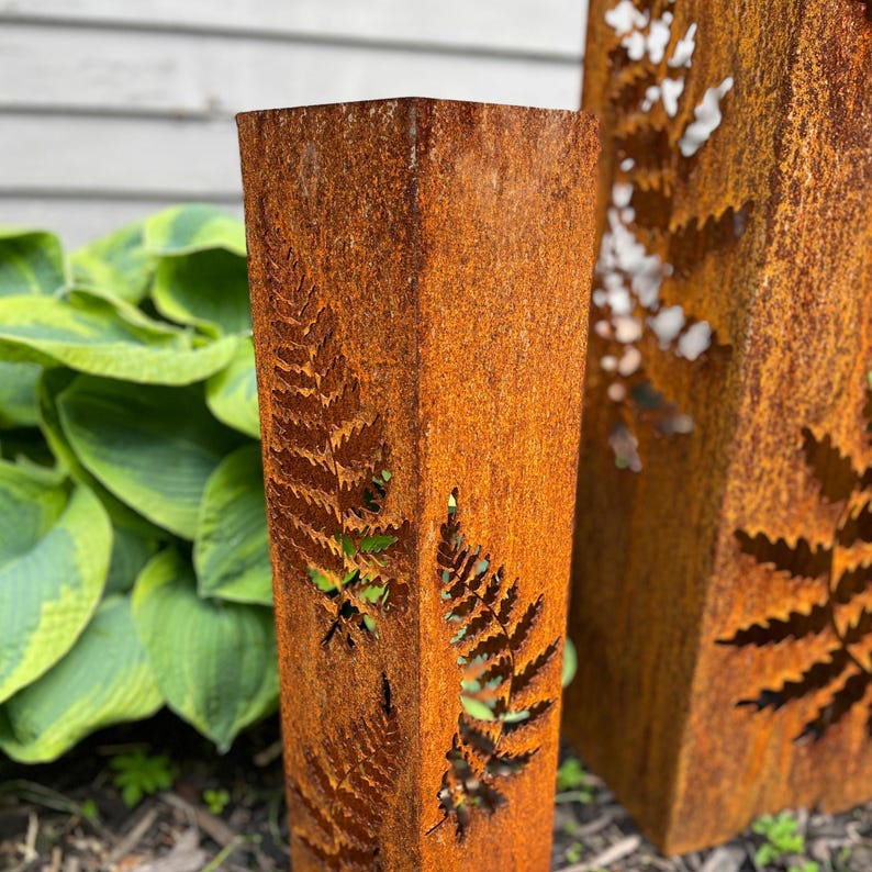 May include: Two rusty metal garden stakes with a fern design cut out. The stakes are brown and orange with a rough texture.