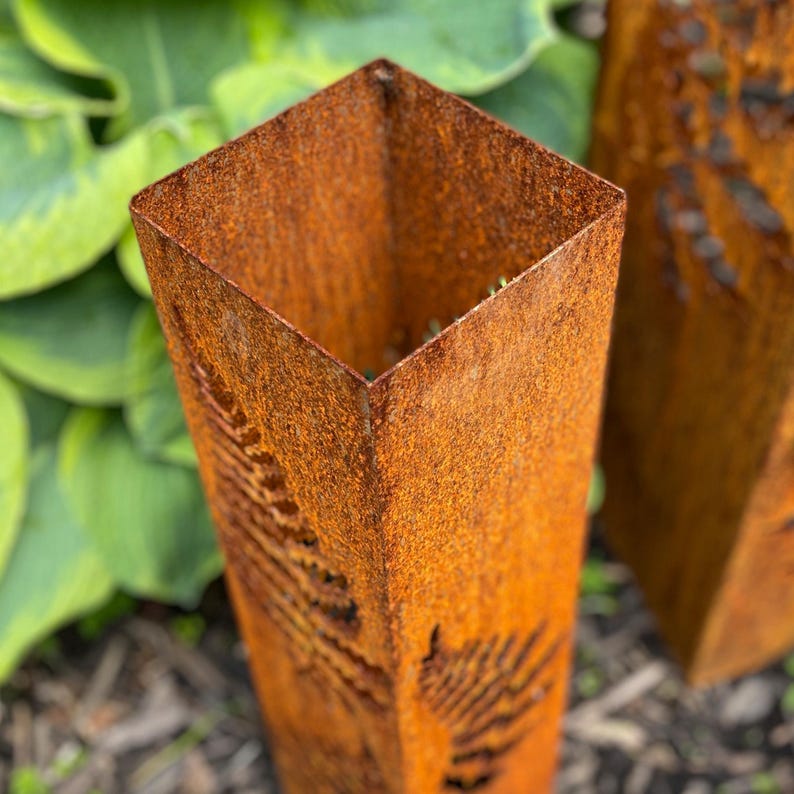 May include: A rusty metal planter with a fern design. The planter is square and has a rustic look.