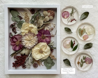 May include: A white 11"x14" shadow box containing a pressed floral arrangement with cream, burgundy, and green dried botanicals, accompanied by four circular coasters featuring embedded flower petals and leaves, labeled Circle Coasters.