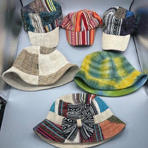 May include: A collection of six colorful, patchwork hats. The hats feature various patterns and designs, including stripes, tie-dye, and geometric shapes. The hats are made of fabric and have a brim or visor.