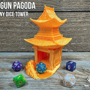 May include: A bright orange 3D-printed dice tower shaped like a Shogun Pagoda, featuring a multi-tiered roof and an open entrance. The text SHOGUN PAGODA TINY DICE TOWER is visible at the top. Several multi-sided gaming dice are placed around the base.