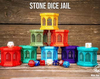 May include: A collection of seven hexagonal dice jails in yellow, green, red, teal, blue, purple, and cyan, arranged in a pyramid. The structures feature arched window cutouts. Several multi-sided dice are placed in front and on top.