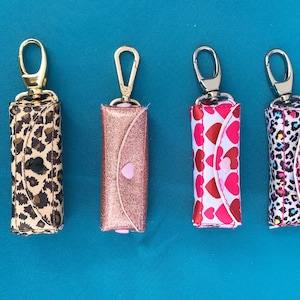 May include: Four small zippered pouches with key rings. The pouches are made of fabric and have different patterns: leopard print, pink glitter, hearts, and a multi-colored animal print.